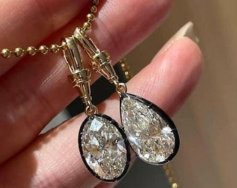 Puede incluir: Pendientes de oro con grandes colgantes de diamantes brillantes, de forma ovalada y de pera. Los diamantes están engastados en biseles negros y cuelgan de una fina cadena de oro.
