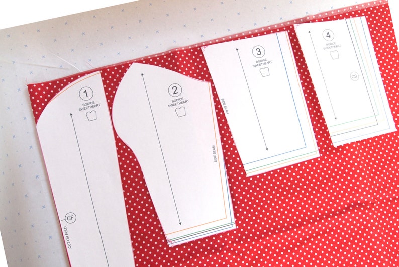 May include: Four white paper patterns for sewing a sweetheart bodice. The patterns are numbered 1 through 4 and are laid out on a red fabric with white polka dots.