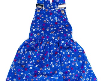May include: A blue floral print overall dress with adjustable straps. The dress features a pattern of small white, pink, and orange flowers. The straps have metal hardware.