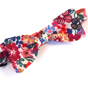 May include: A floral patterned bow tie with red, pink, blue, and white flowers on a cream background.