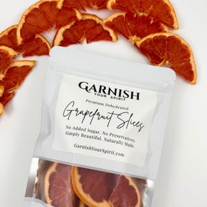 May include: A package of dehydrated grapefruit slices with the text "GARNISH YOUR SPIRIT" and "Grapefruit Slices". The slices are a vibrant orange-red color and are arranged around the package. The text on the package reads "No Added Sugar. No Preservatives. Simply Beautiful. Naturally Made."