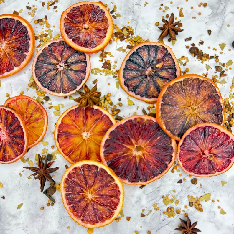 Bulk Dehydrated Blood Orange Slices - Dried Ruby Red Orange for Cocktails and Decor 80+ pieces on a tables spread out with herbs and spices in a very festive fall theme