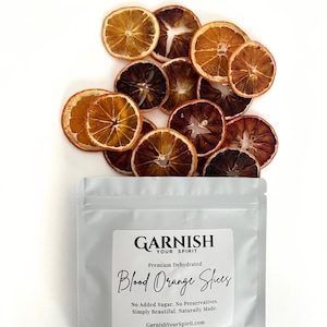 May include: Dehydrated blood orange slices arranged on a white surface, with a package of "Garnish Your Spirit" blood orange slices. The slices are various shades of brown and orange. The package text reads "Premium Dehydrated Blood Orange Slices."