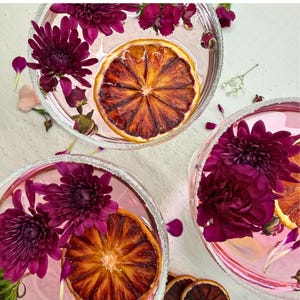 drink decor of Bulk Dehydrated Blood Orange Slices - Dried Ruby Red Orange for Cocktails and Decor 80+ pieces on a tables spread out with flowers and petals and spices