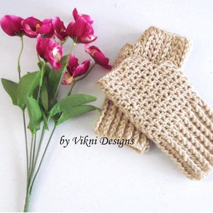 May include: A pair of beige crocheted fingerless gloves with a ribbed cuff. The gloves are on a white surface with a bouquet of pink flowers.