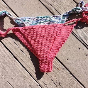 May include: A pink crocheted bikini bottom with a white and green crocheted top layer.