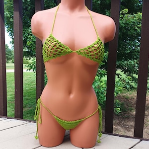 May include: A lime green crochet bikini set. The top is a triangle style with halter straps. The bottoms are a string bikini style with tie sides. The crochet has an open, net-like pattern. The set is displayed on a mannequin.