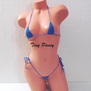May include: A blue crocheted bikini set with a triangle top and a string bottom. The bikini is on a mannequin. The text "Tiny Pansy" is printed on the mannequin's stomach.