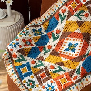 May include: A colorful, crocheted blanket with a patchwork design. The blanket features squares of blue, orange, yellow, and brown, adorned with floral and butterfly motifs. The edges are finished with a dotted border.