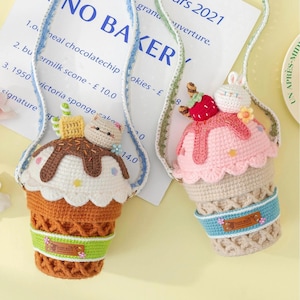 Puede incluir: Dos bolsos de cono de helado de ganchillo hechos a mano. Uno es marrón con un gato encima, el otro es rosa con un conejito. Ambos tienen una correa azul y verde. Los bolsos están decorados con una banda verde y una pequeña etiqueta que dice "HAND MADE".