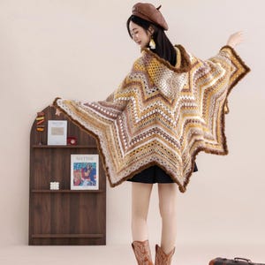 Puede incluir: Poncho de ganchillo con forma de estrella, con capucha, en tonos marrón, crema y amarillo. El poncho tiene un ribete de piel y se lleva con una boina marrón y botas de vaquero. El estilo general es bohemio.