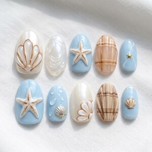 Könnte beinhalten: Ein Set aus zehn künstlichen Nägeln mit Strandmotiv. Die Nägel zeigen Designs von Muscheln, Seesternen und Karomustern in Weiß, Blau und Braun. Einige Nägel haben 3D-Verzierungen.