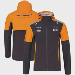 Puede incluir: Chaqueta negra y naranja del equipo McLaren de Fórmula 1 con capucha. La chaqueta presenta el logotipo de McLaren y los logotipos de los patrocinadores. La chaqueta tiene una cremallera completa y detalles en naranja en los hombros y la capucha.