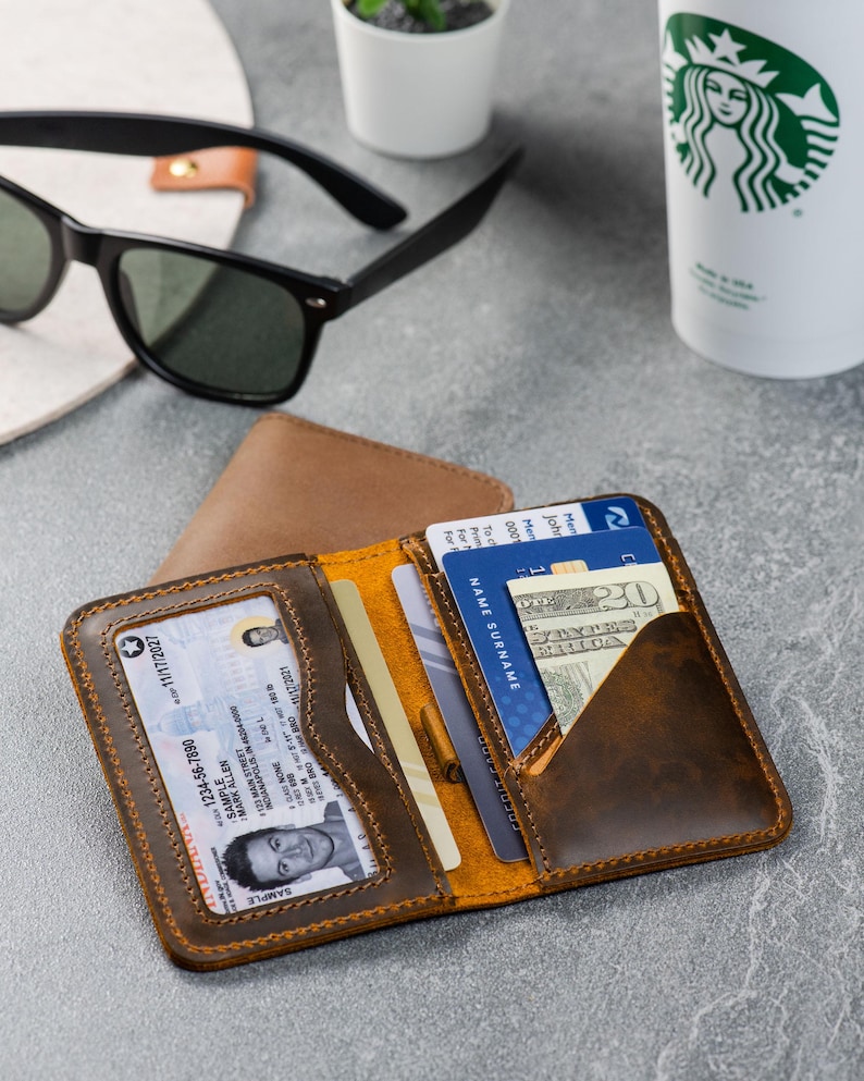 Slim leather front-pocket wallet in amber brown displayed with sunglasses on a gray surface