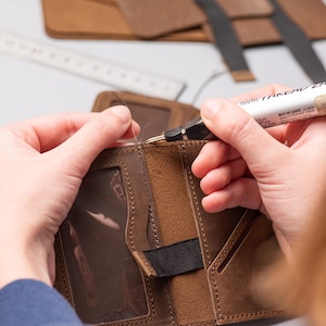 Hands crafting and stitching the men’s leather wallet during production