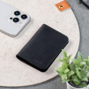 Black minimalist wallet next to iPhone and plant on a desk