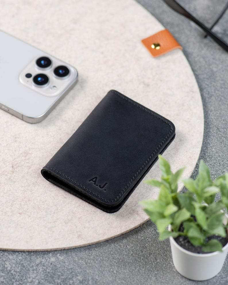 Black minimalist wallet next to iPhone and plant on a desk