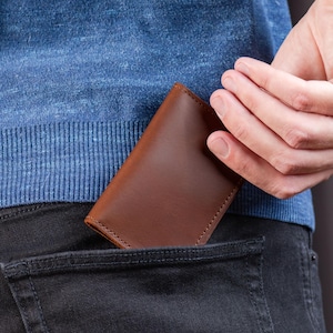 Man sliding cognac leather wallet into his front jeans pocket