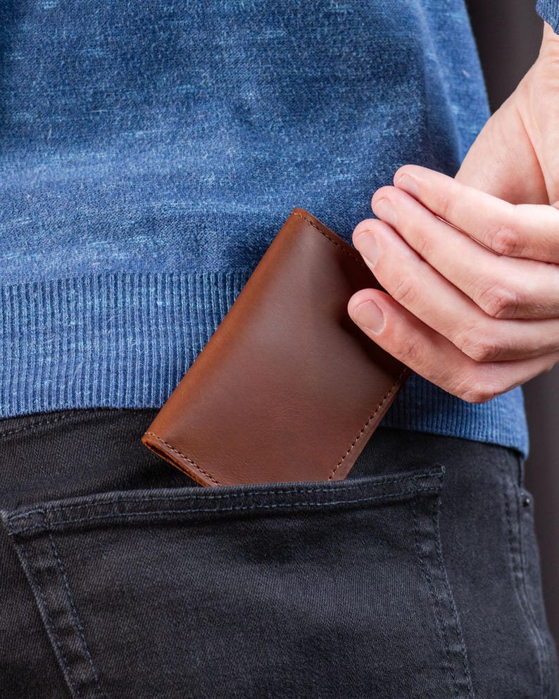 Man sliding cognac leather wallet into his front jeans pocket