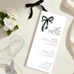 May include: A white menu card with a black bow illustration at the top. The text "The MENU" is displayed in elegant script. The menu lists starters, main courses, and desserts, including Seared Scallops and Salted Caramel Cheesecake.
