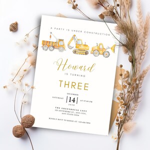 Puede incluir: Una invitación de cumpleaños blanca con texto dorado e ilustraciones de acuarela de vehículos de construcción. La invitación dice "A Party is Under Construction" e incluye el nombre "Howard" y la edad "THREE".