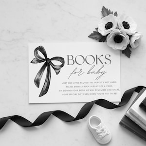 Puede incluir: Una invitación de baby shower en blanco y negro con el texto "BOOKS for baby" y un lazo decorativo. La invitación está acompañada de un zapato de bebé blanco, una cinta negra y un ramo de flores blancas.