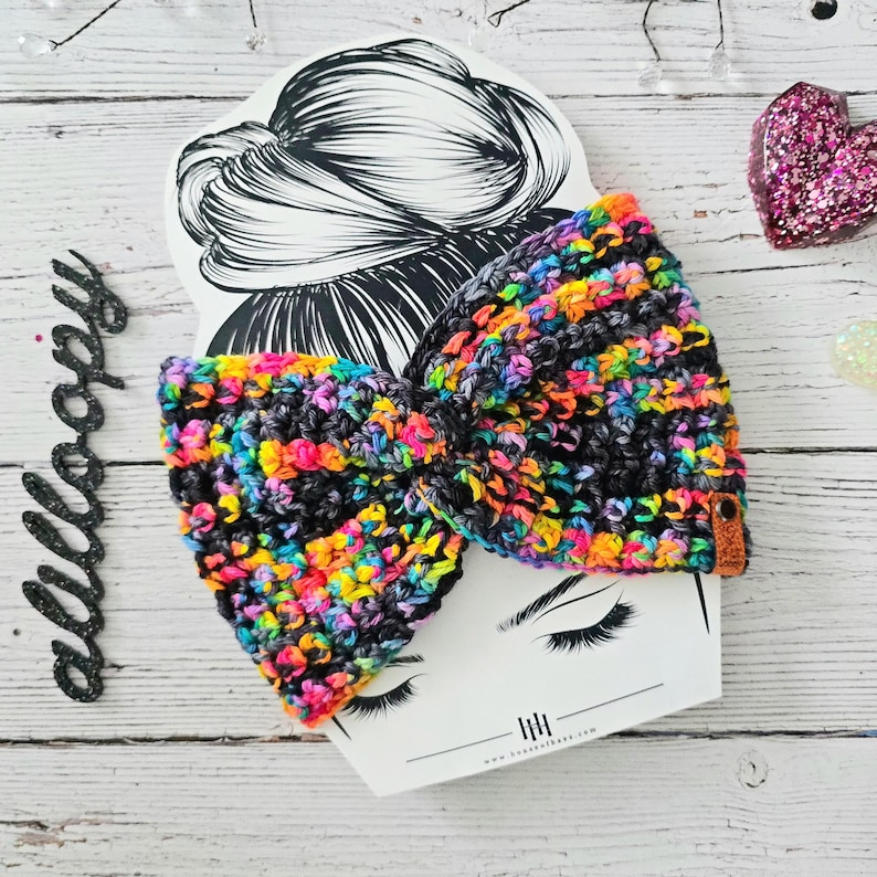Puede incluir: Una diadema de crochet colorida con fondo negro y rayas arco&iacute;ris. La diadema est&aacute; atada en un lazo y se muestra sobre un fondo blanco.