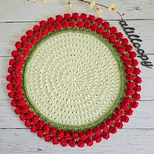 Peut inclure: Un dessous de plat crocheté avec un centre vert et blanc et une bordure de pompons rouges.