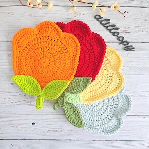 Puede incluir: Cuatro posavasos de ganchillo con forma de flor en tonos naranja, rojo, amarillo y azul. Los posavasos están apilados, con el naranja en la parte superior. Cada posavasos tiene una hoja de ganchillo verde unida a la parte inferior.