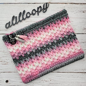 May include: A pink, white, and gray crocheted zippered pouch with a silver glitter thread. The pouch has a small black leather tag with the text "A Little Loopy" on it.