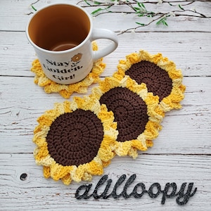 May include: Four crocheted sunflower coasters in shades of yellow and brown. The coasters are arranged in a semi-circle around a white mug with the text "Stay Golden Girl!" on it.