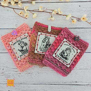 Pode incluir: Tr&ecirc;s capas de livros de croch&ecirc; feitas &agrave; m&atilde;o em tons de rosa e castanho. Cada capa apresenta um r&oacute;tulo impresso com uma ilustra&ccedil;&atilde;o vintage de uma mulher lendo e texto humor&iacute;stico: "Crying Over Book Boyfrie", "If I'm Read You Shou Shhhh", e "Leave Me Alone I'm Reading".
