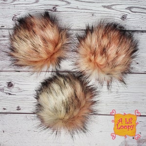 May include: Three faux fur pom poms in different colour combinations. The pom poms are made of black, white and peach coloured fur.