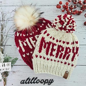 May include: Two knitted winter hats with pom poms. One hat is white with red "Merry" lettering and the other is red with white hearts and "Merry" lettering.