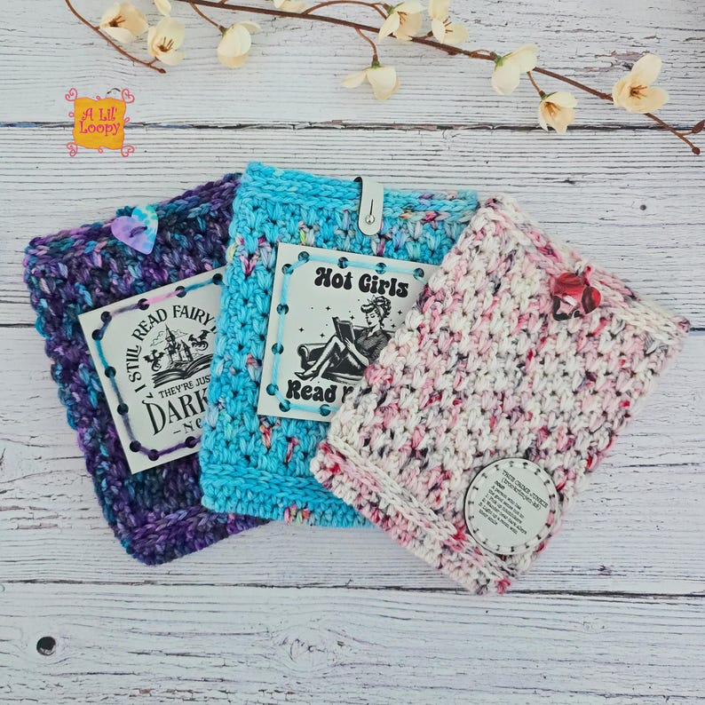 Pode incluir: Tr&ecirc;s capas de livros de croch&ecirc; feitas &agrave; m&atilde;o em tons de roxo, azul e rosa. Cada capa tem uma etiqueta decorativa com texto e um fecho de bot&atilde;o. As etiquetas dizem "I Still Read Fairy Dark" e "Hot Girls Read".