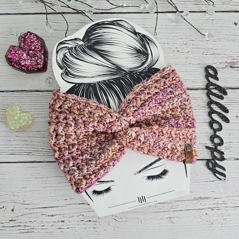 Puede incluir: Una diadema de crochet rosa y blanca con un lazo. La diadema est&aacute; sobre un fondo blanco con un dibujo de la cabeza de una mujer.