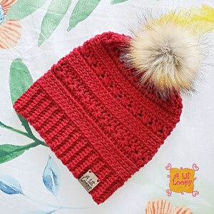 May include: Red crocheted beanie with a faux fur pom pom. The beanie has a label that says "A Lil' Loopy".