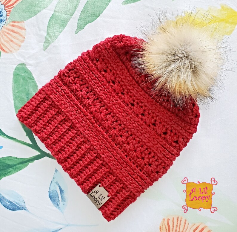 May include: Red crocheted beanie with a faux fur pom pom. The beanie has a label that says "A Lil' Loopy".