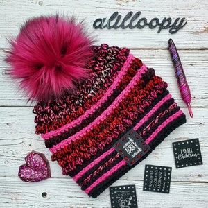 May include: A pink and black crocheted beanie with a large pink pom pom. The beanie has a black leather patch with the text "amuck amuck amuck" on it. There are also several other black leather patches with text on them, including "I smell children", "Another glorious morning makes me sick!" and "If it isn't a bunch of Hocus Pocus".