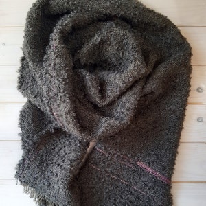 May include: A dark gray fuzzy scarf with a pink stripe woven into the fabric. The scarf has a fringe on the bottom edge.