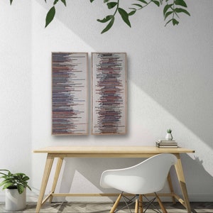 May include: Two abstract wall art pieces with a vertical pattern of colorful lines in shades of red, pink, blue, and gray. The pieces are framed in natural wood and are hung on a white wall.