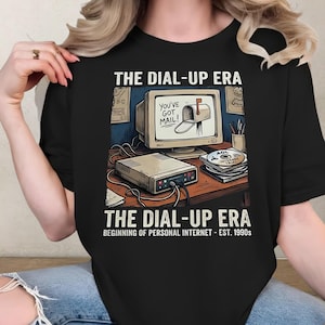 Może przedstawiać: Czarny t-shirt z grafiką retro komputera i napisem "THE DIAL-UP ERA". Grafika zawiera monitor z skrzynką pocztową, modem i płyty CD AOL. Widoczny jest również napis "YOU'VE GOT MAIL!"