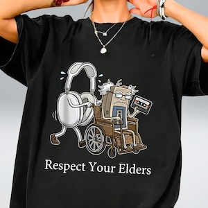 May include: Black t-shirt with a cartoon graphic of a computer in a wheelchair holding a cassette tape, and a pair of headphones. The text "Respect Your Elders" is printed below the graphic.