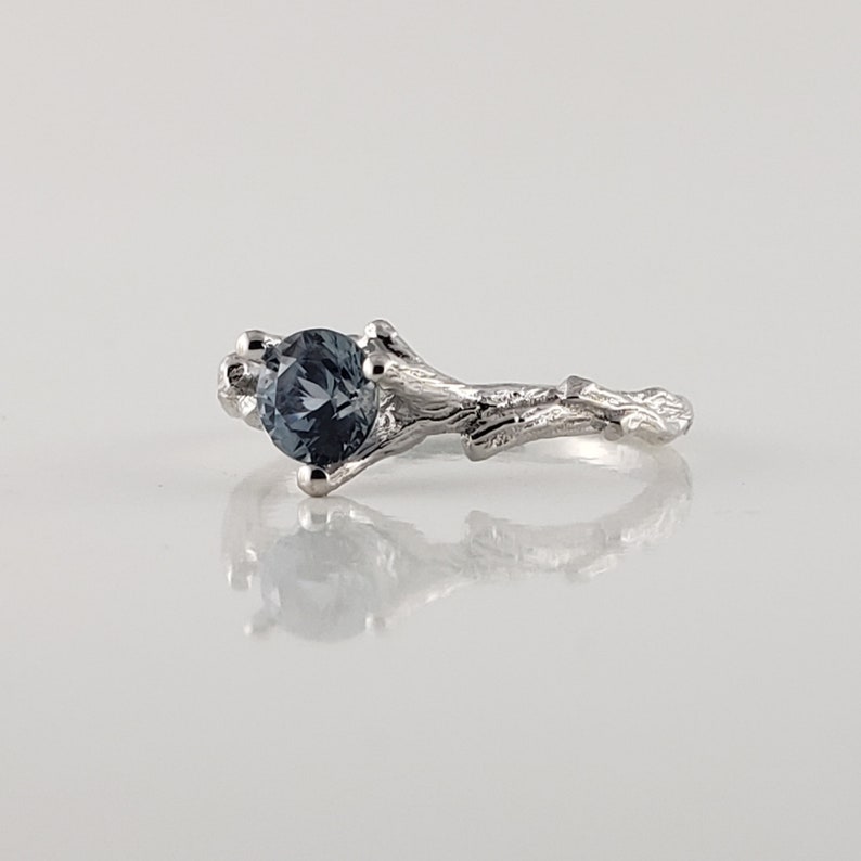 May include: A silver ring featuring a blue gemstone set in a branch-like design.