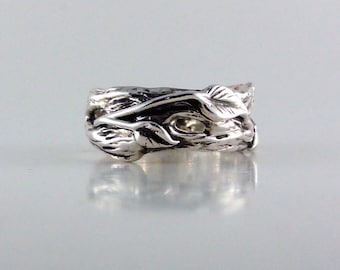 Puede incluir: Un anillo de plata con un diseño de vid con hojas. El anillo está hecho de metal y tiene una superficie texturizada.