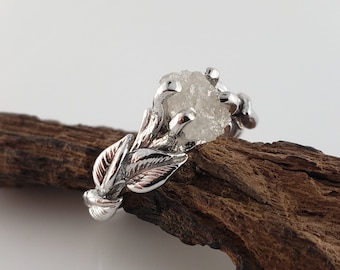 May include: A silver ring with a rough, white diamond set in a leaf design.