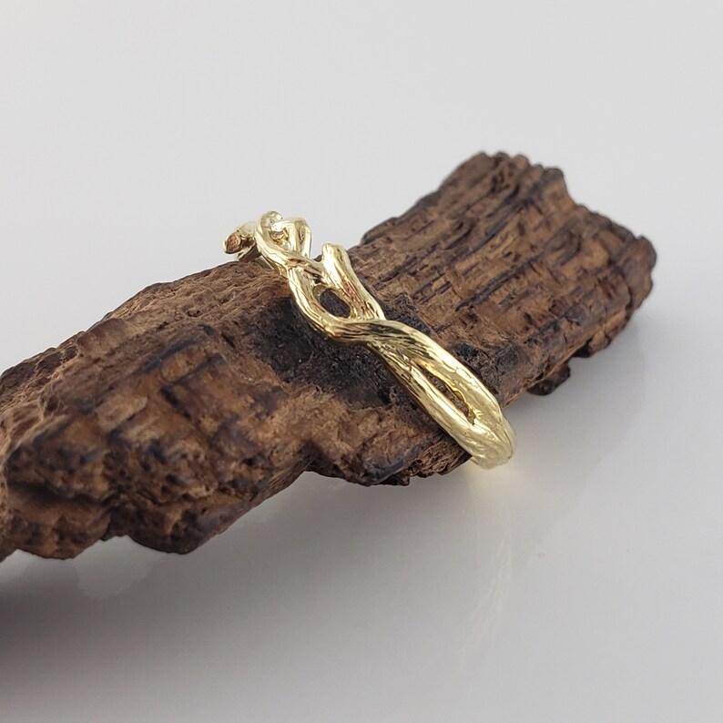 May include: A gold ring with a twisted, branch-like design. The ring is displayed on a piece of dark brown wood.