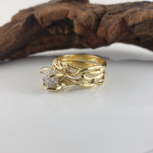 May include: A gold ring set with a large, rough-cut diamond. The band is intricately designed with a branch-like pattern.