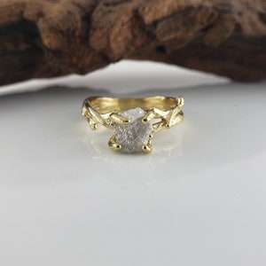 May include: A gold ring with a rough, white diamond set in a branch-like design.
