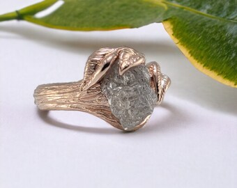 May include: A rose gold ring featuring a rough, grey diamond set in a leaf design.